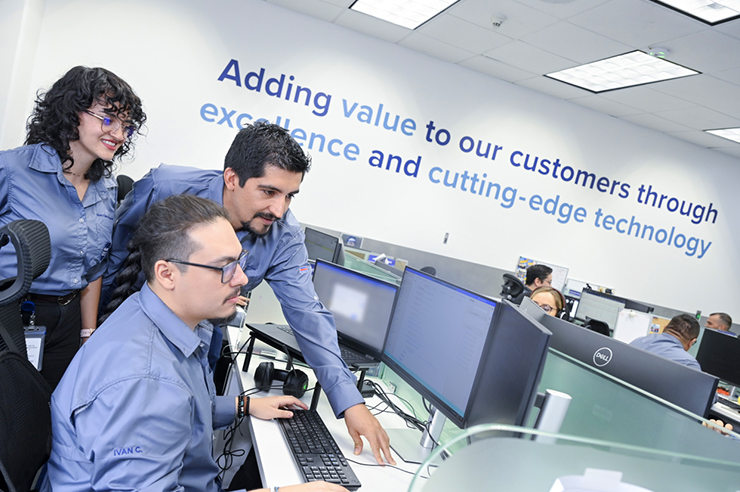 Coworkers grouped together and looking at a monitor in an office setting.