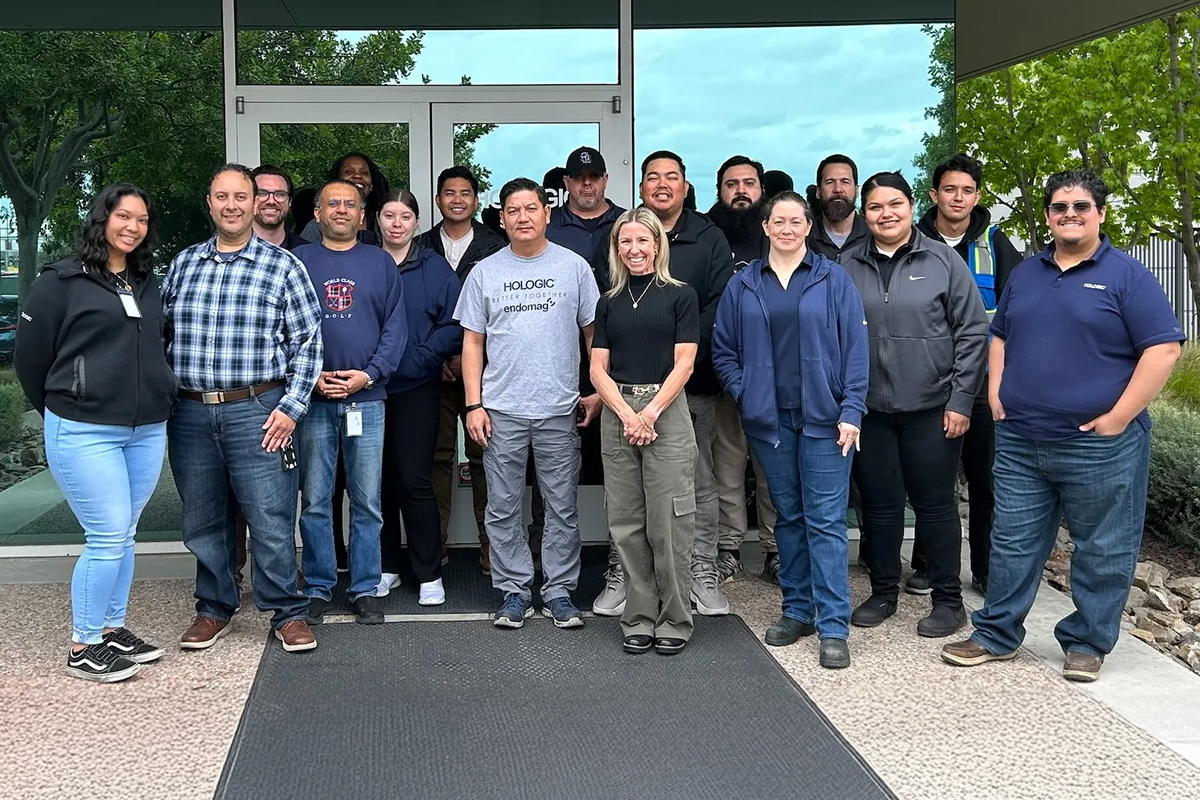 Group of people stand together in front of a sign reading "Hologic".