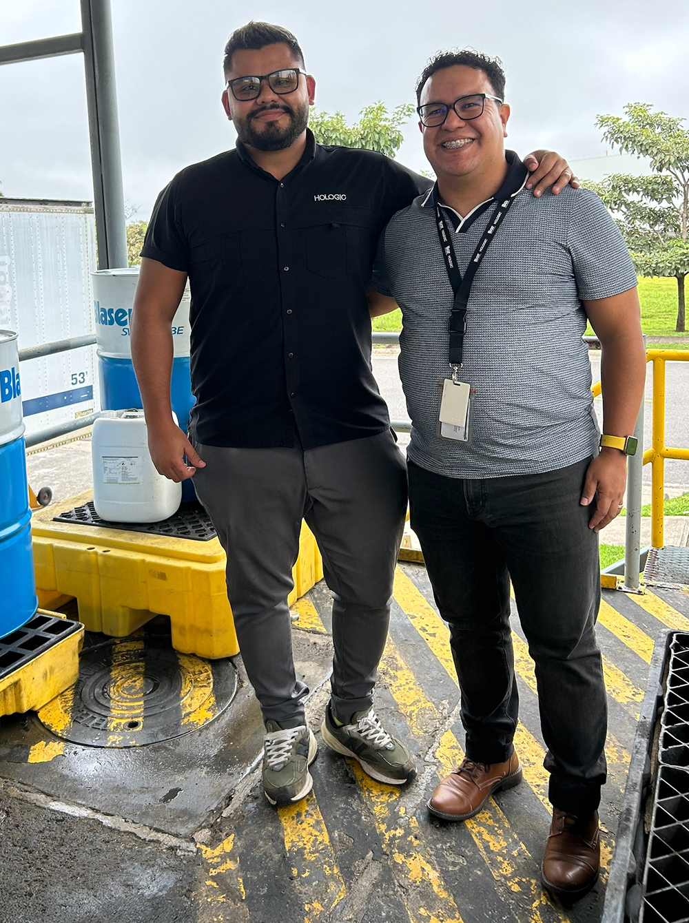 Two individuals stand next to each other outside in the sun.