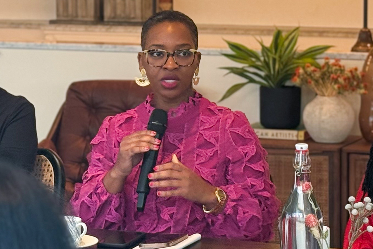 Three women sit at a table with one speaking into a microphone.