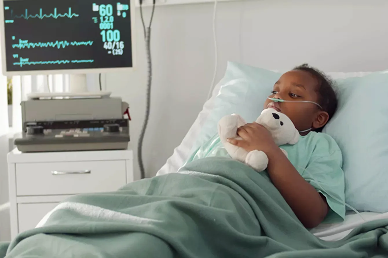 Image of a child resting at a hospital bed while holding a teddy bear toy