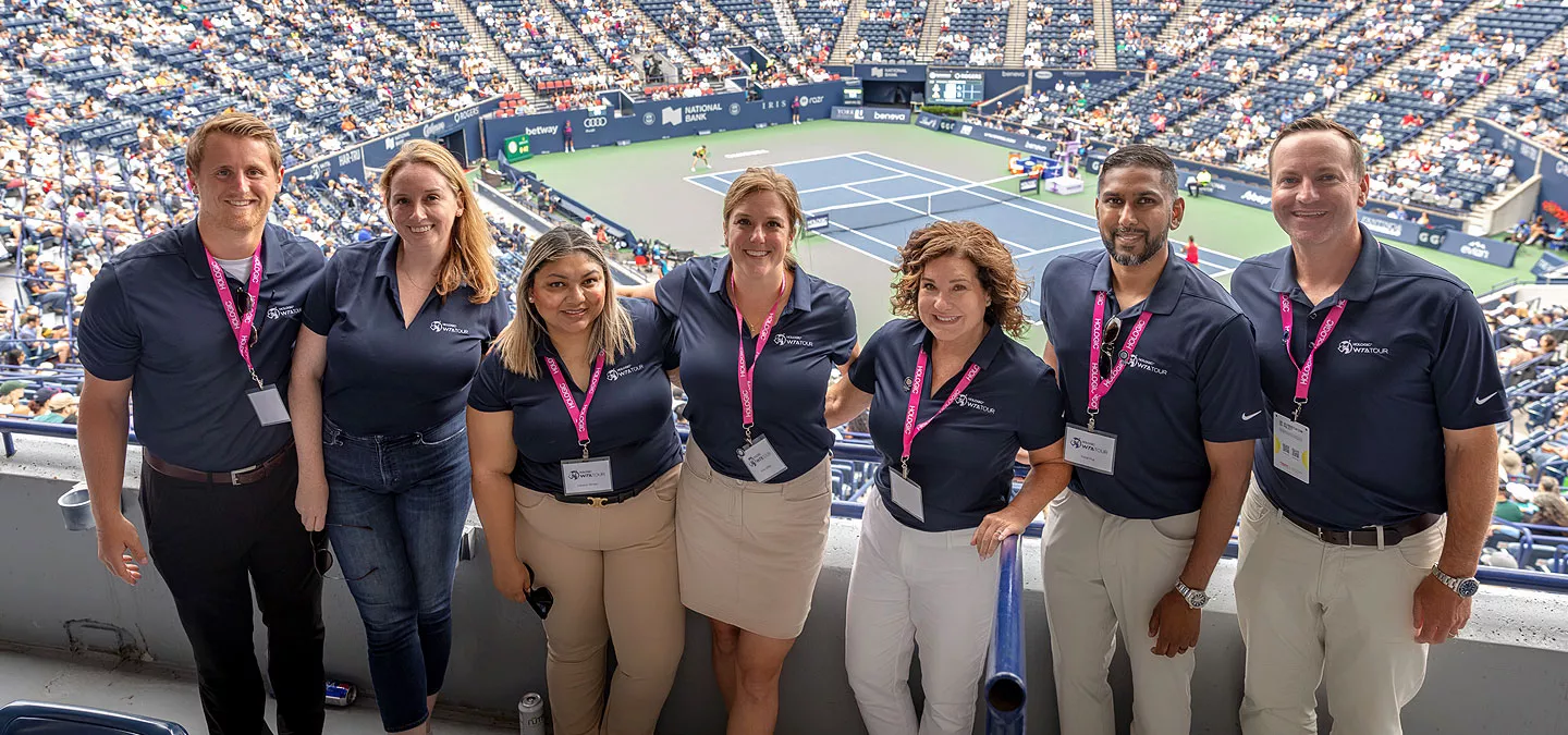 Group photo with tennis stadium and court in background.