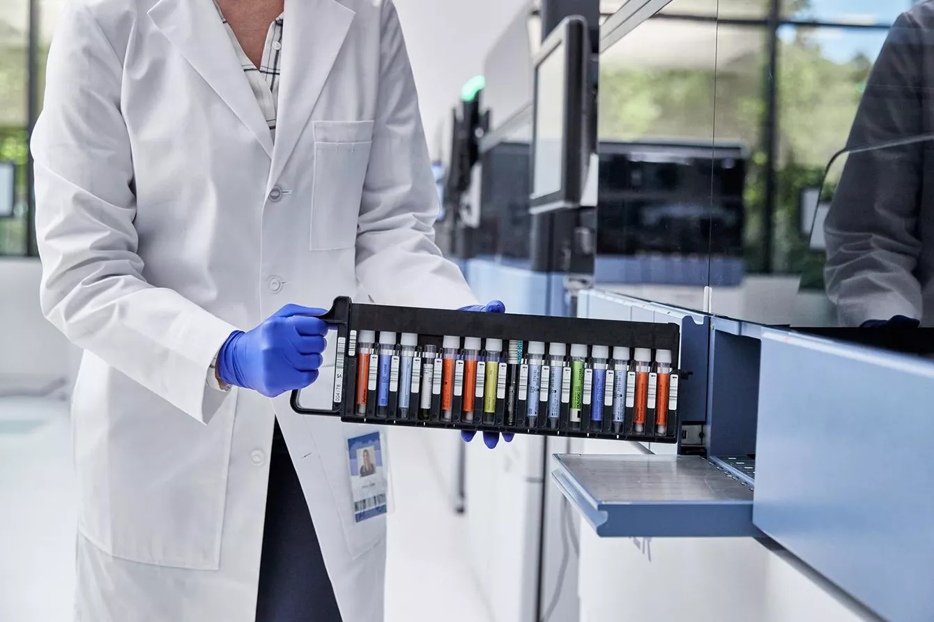 Lab technician loading vial tray into medical equipment in lab setting.